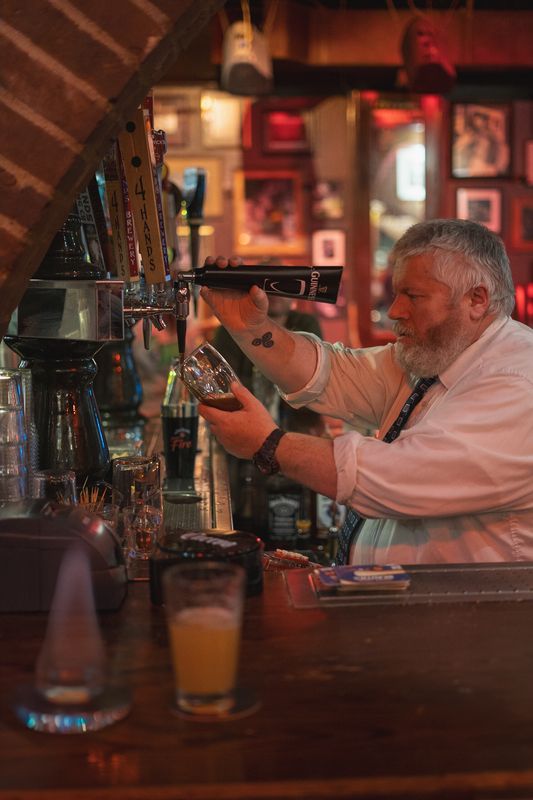 Bartender carefully pouring a dark beer at a warmly lit bar