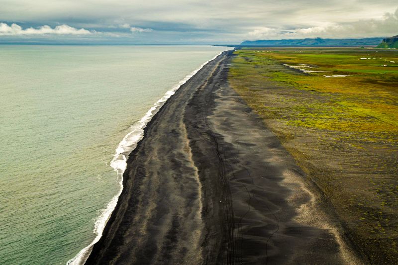 Aerial view of a long black sand beach with green coastal land
