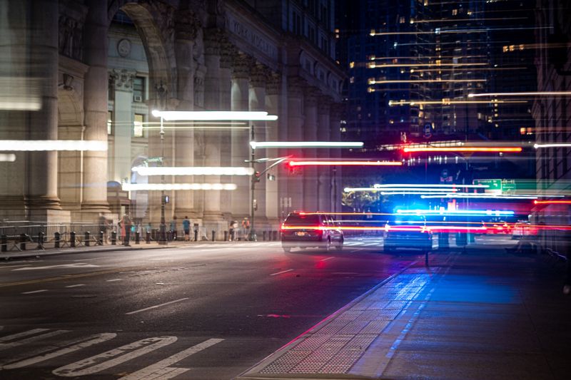 Night city street with long-exposure light trails and flashing emergency lights