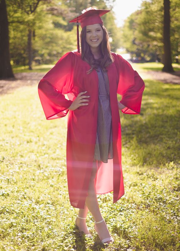 Smiling graduate in a red cap and gown standing in golden backlight
