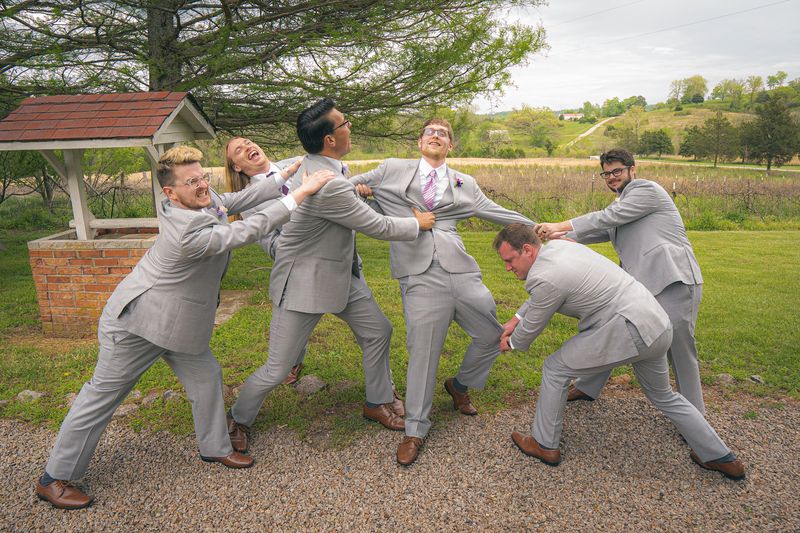 Groomsmen in gray suits playfully pulling the groom in different directions
