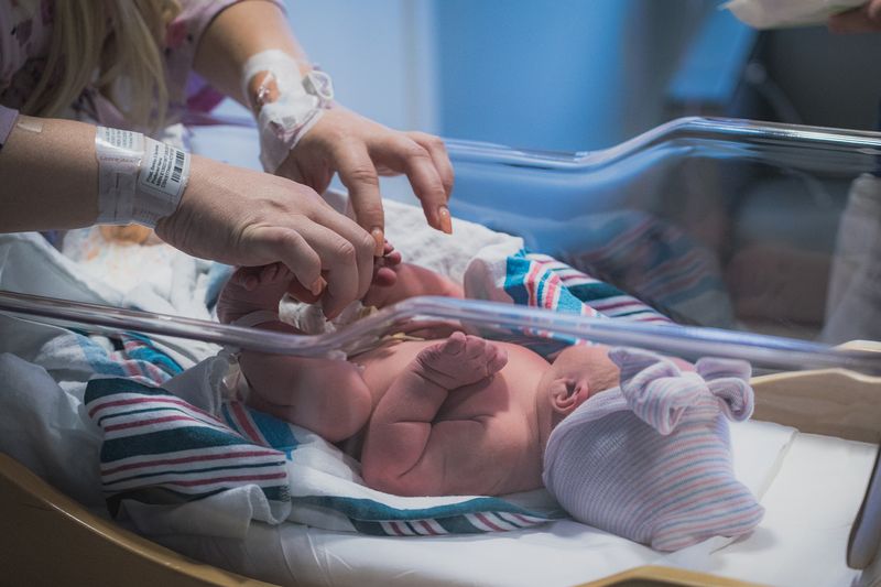 Newborn baby in a hospital bassinet with a parent's hands gently touching the baby's feet