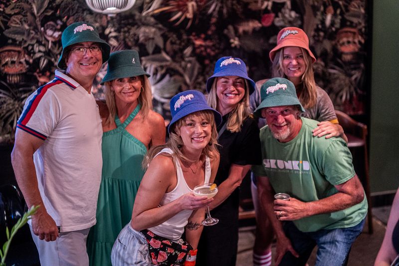 Six smiling guests wearing matching bucket hats at a bar event