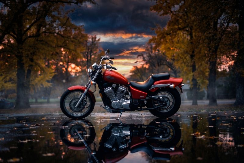 Red cruiser motorcycle parked in a wet autumn park at sunset with its reflection below