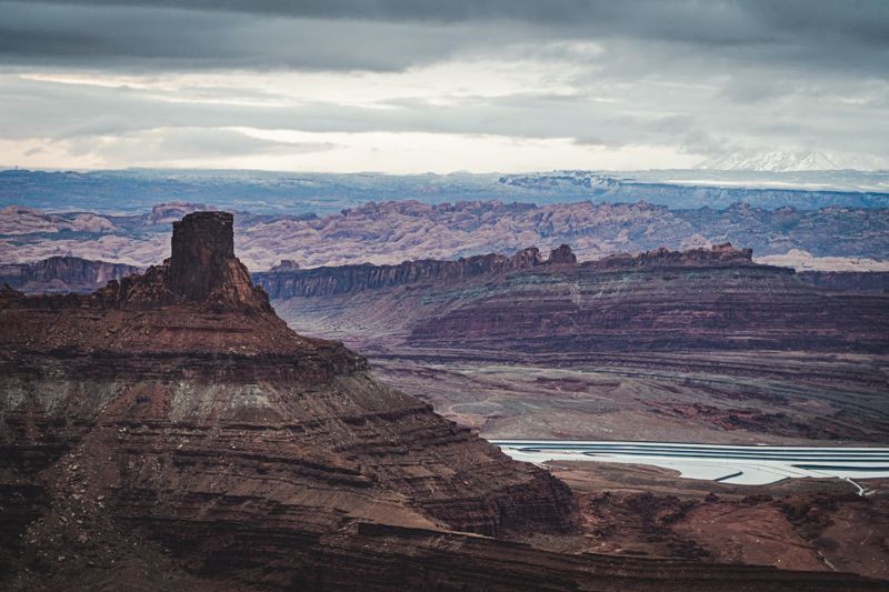 Layered red rock canyon landscape with a tall butte and snowy mountain in the distance