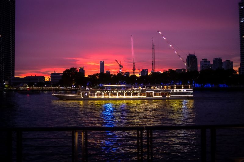 Illuminated river cruise boat on the water beneath a vivid pink and purple sunset with city skyline