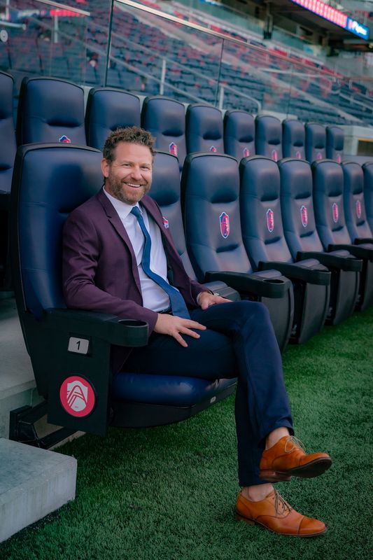 Smiling executive in a burgundy blazer seated in a stadium seat