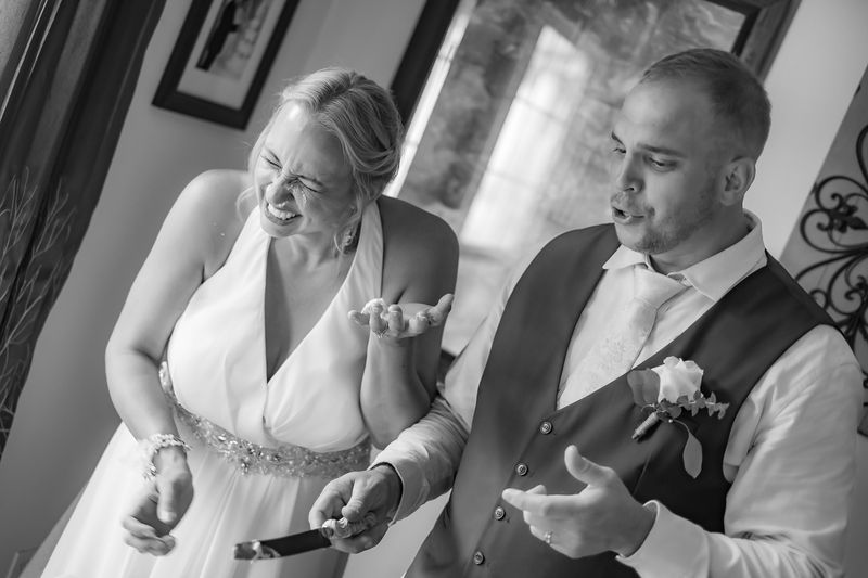 Black and white photo of a bride laughing with frosting on her nose beside her groom
